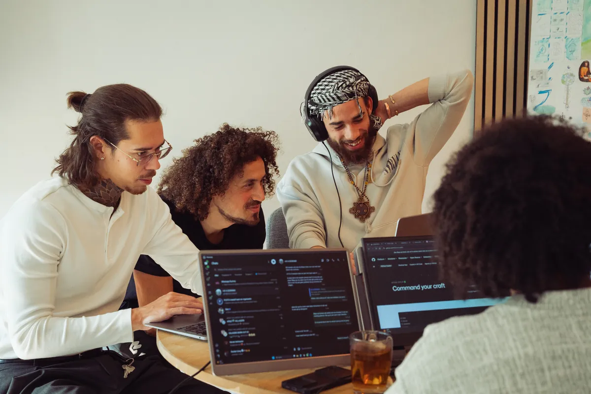 Drie makers kijken samen lachend naar een laptop aan een ronde tafel