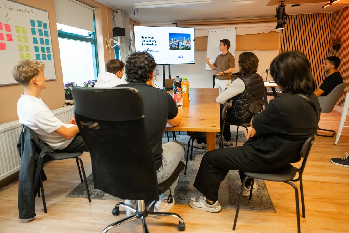 Een spreker geeft een presentatie aan een groep rond de lange tafel