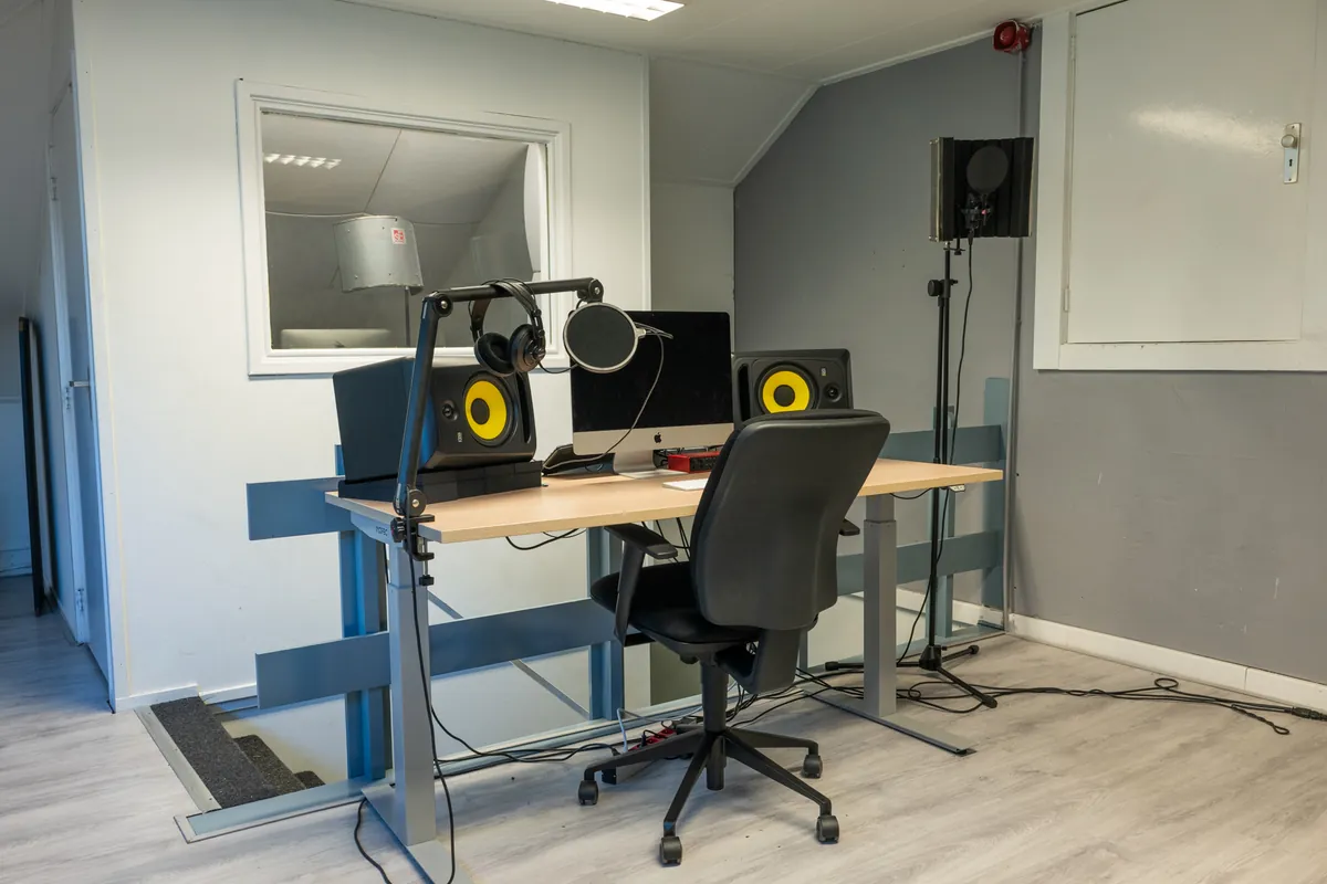 Een bureau met studiomonitoren, een microfoon met popfilter en een iMac in de studio